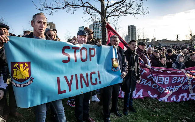 Angry NFL fans holding protest signs outside a stadium.